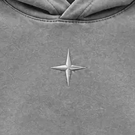 Close-up of the compass stitched in grey thread at the centre chest.
